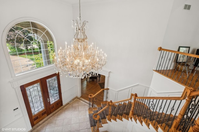 tiled foyer entrance featuring stairway, visible vents, an inviting chandelier, french doors, and a decorative wall