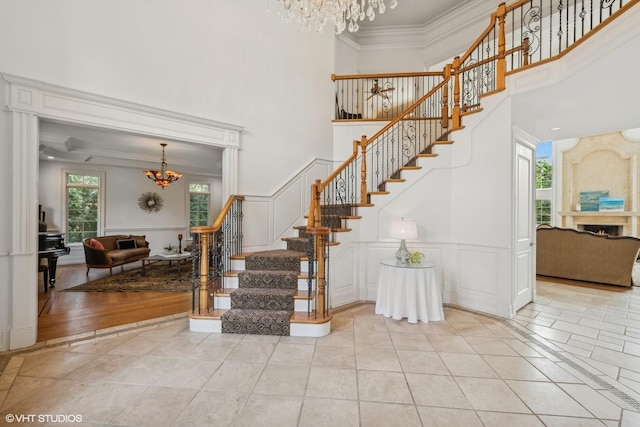 stairway featuring a warm lit fireplace, tile patterned flooring, crown molding, a decorative wall, and a notable chandelier