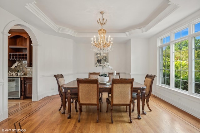 dining area with baseboards, beverage cooler, a chandelier, a tray ceiling, and light wood-style flooring