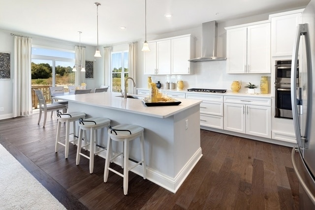 kitchen featuring a center island with sink, wall chimney exhaust hood, white cabinets, and hanging light fixtures