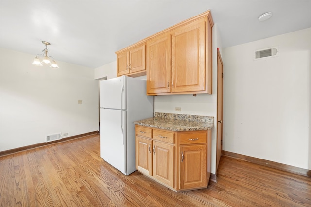 kitchen featuring hanging light fixtures, an inviting chandelier, light stone counters, white refrigerator, and light hardwood / wood-style floors