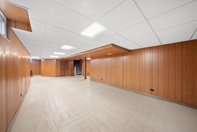 basement with a drop ceiling and wooden walls