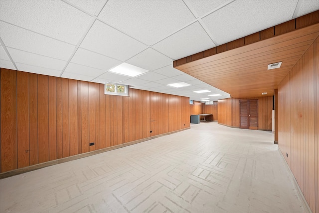 basement with a paneled ceiling and wood walls