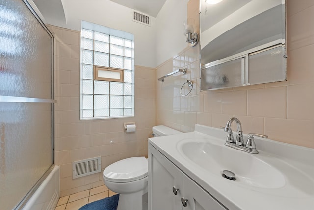 full bathroom with vanity, tile patterned floors, bath / shower combo with glass door, toilet, and tile walls