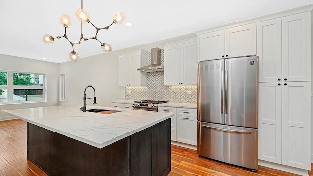 kitchen with appliances with stainless steel finishes, wall chimney exhaust hood, light hardwood / wood-style flooring, white cabinetry, and hanging light fixtures