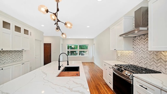 kitchen featuring wall chimney range hood, white cabinets, light hardwood / wood-style floors, stainless steel range with gas cooktop, and hanging light fixtures