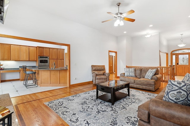 living room featuring sink, a towering ceiling, ceiling fan, and light wood-type flooring