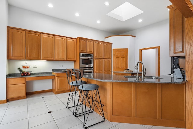 kitchen featuring sink, a breakfast bar area, dark stone countertops, double oven, and built in desk