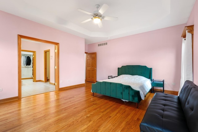 bedroom featuring a raised ceiling, stacked washer and clothes dryer, ceiling fan, and light hardwood / wood-style flooring