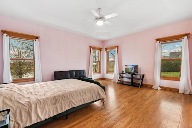 bedroom with a tray ceiling, ceiling fan, and light hardwood / wood-style flooring