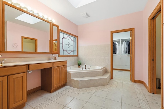 bathroom featuring tiled tub, vanity, tile patterned flooring, and a skylight