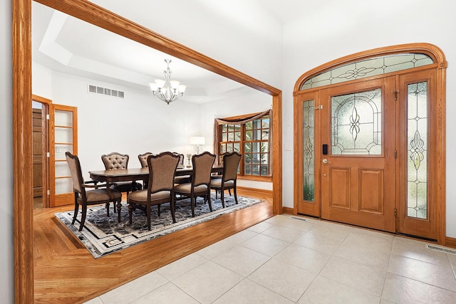 tiled entryway with a raised ceiling and a notable chandelier