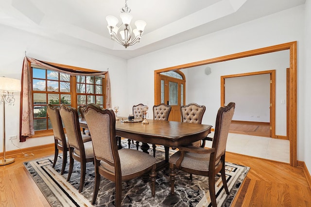 dining area with an inviting chandelier, wood-type flooring, and a raised ceiling