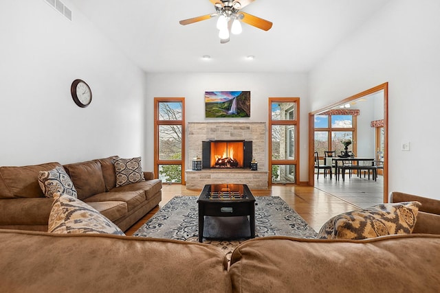 living room featuring a stone fireplace, a wealth of natural light, ceiling fan, and light hardwood / wood-style floors