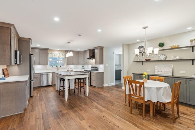 kitchen with pendant lighting, wall chimney range hood, stainless steel appliances, wood-type flooring, and a kitchen island