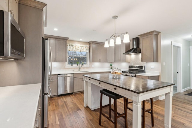 kitchen with sink, decorative light fixtures, appliances with stainless steel finishes, dark hardwood / wood-style flooring, and wall chimney range hood