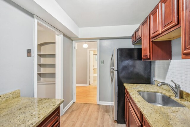 kitchen with decorative backsplash, light wood-type flooring, light stone countertops, and sink