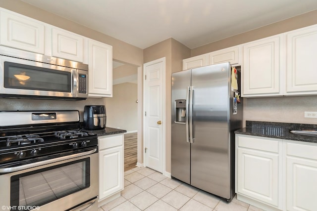 kitchen featuring dark stone counters, white cabinetry, light tile patterned floors, and stainless steel appliances