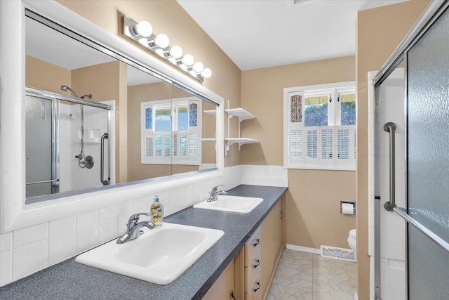 bathroom featuring vanity, toilet, a shower with shower door, and backsplash