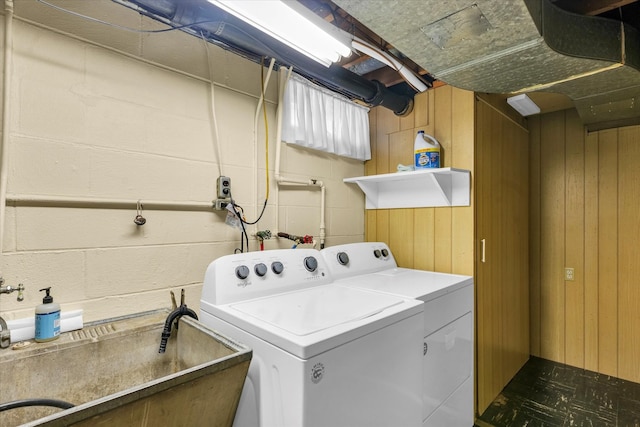 clothes washing area with washer and clothes dryer, sink, and wooden walls