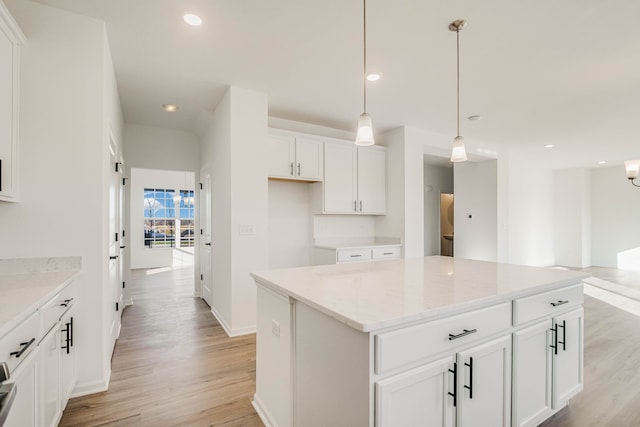 kitchen featuring light stone countertops, pendant lighting, light hardwood / wood-style flooring, a center island, and white cabinetry