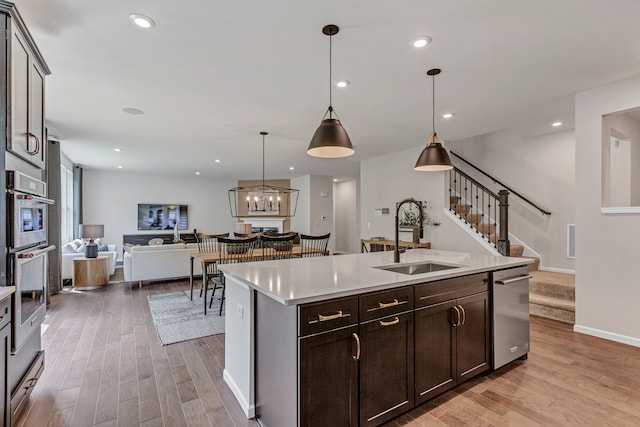 kitchen with sink, light hardwood / wood-style flooring, stainless steel dishwasher, an island with sink, and pendant lighting