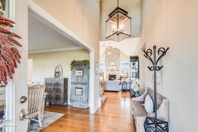 foyer entrance with a high ceiling, light wood-type flooring, a fireplace, ceiling fan with notable chandelier, and ornamental molding