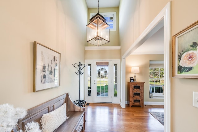 entryway featuring hardwood / wood-style floors, a towering ceiling, an inviting chandelier, and crown molding