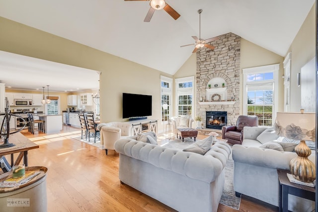 living room with ceiling fan, light hardwood / wood-style floors, a stone fireplace, and high vaulted ceiling