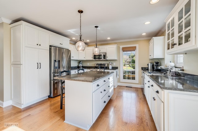 kitchen featuring dark stone counters, sink, appliances with stainless steel finishes, decorative light fixtures, and white cabinetry