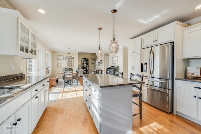 kitchen with a kitchen bar, stainless steel refrigerator with ice dispenser, decorative light fixtures, light hardwood / wood-style floors, and white cabinetry