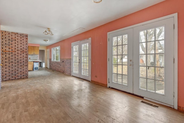 unfurnished living room with french doors, light hardwood / wood-style floors, and brick wall