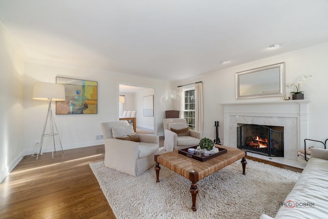 living room with a high end fireplace, wood-type flooring, and ornamental molding