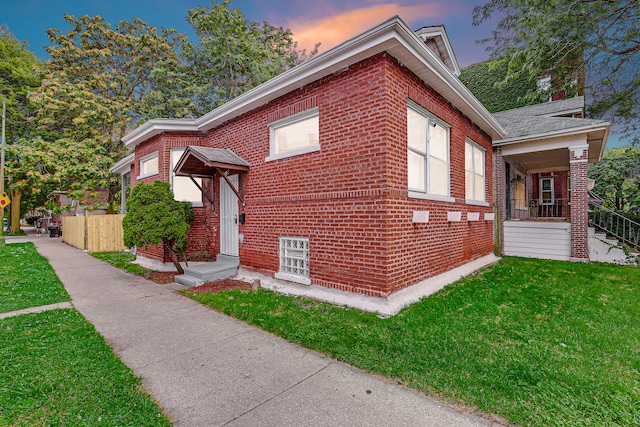 property exterior at dusk with a lawn and covered porch