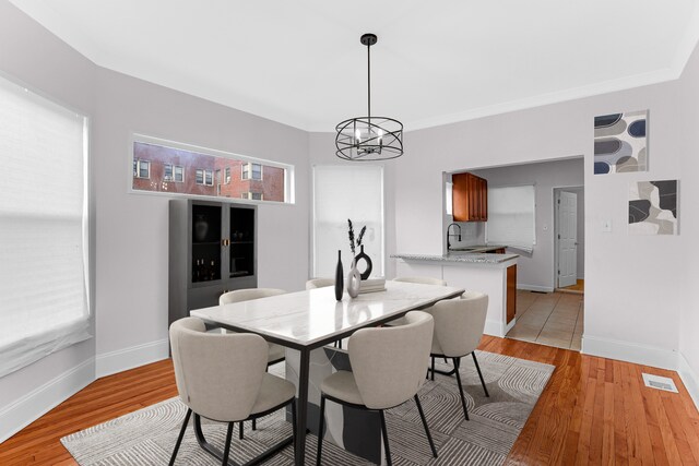 dining space with a notable chandelier, sink, crown molding, and light hardwood / wood-style flooring