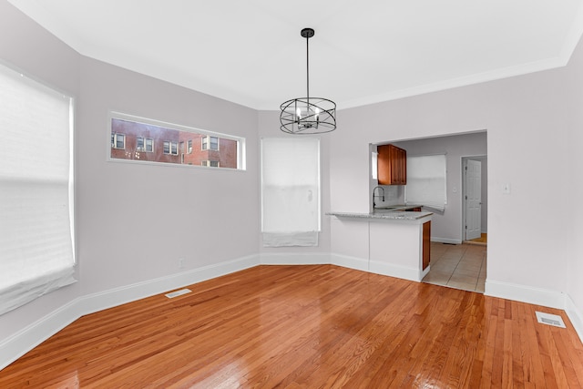 unfurnished dining area with sink, light wood-type flooring, ornamental molding, and a chandelier