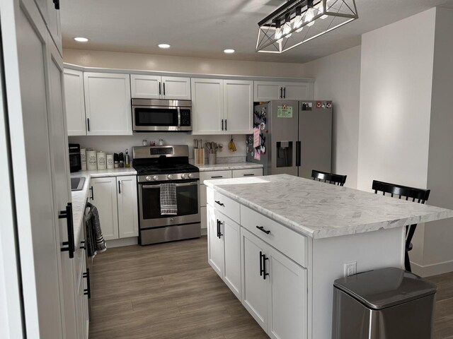 kitchen featuring a center island, white cabinetry, a kitchen bar, wood-type flooring, and stainless steel appliances