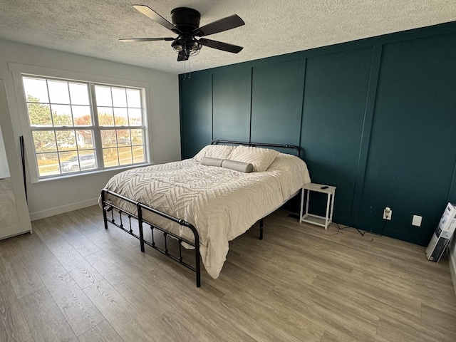 bedroom with ceiling fan, a textured ceiling, and light wood-type flooring