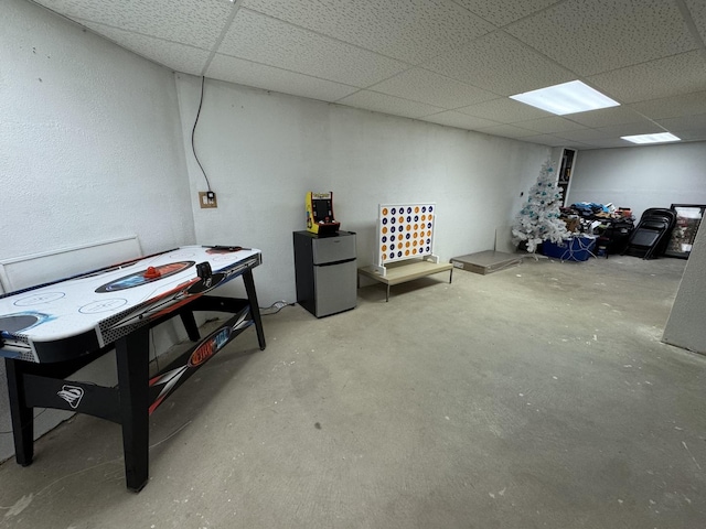 basement with a paneled ceiling and stainless steel refrigerator