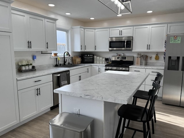 kitchen with sink, a center island, stainless steel appliances, wood-type flooring, and white cabinets