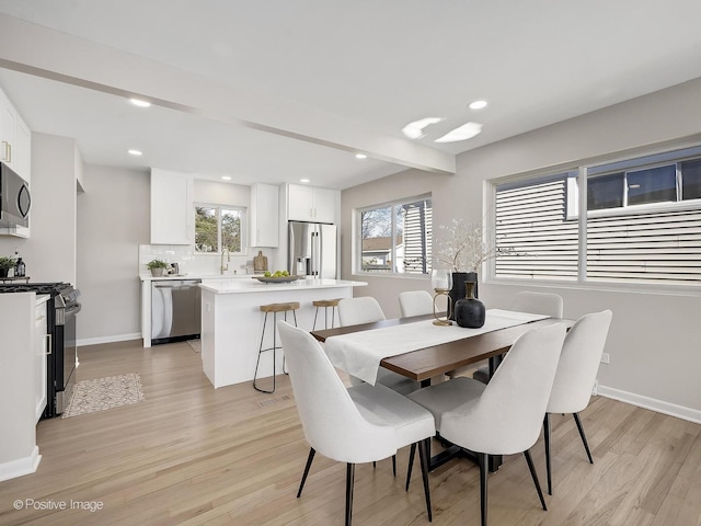 dining area with sink, plenty of natural light, light hardwood / wood-style floors, and beamed ceiling