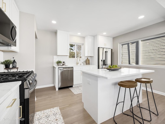 kitchen with sink, appliances with stainless steel finishes, white cabinetry, a kitchen breakfast bar, and a kitchen island