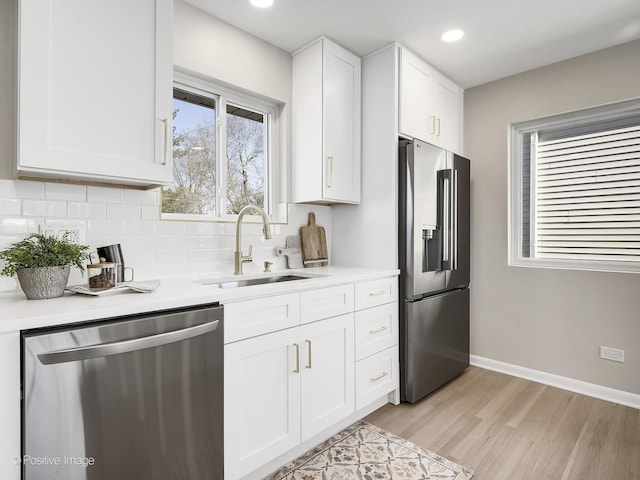 kitchen featuring tasteful backsplash, sink, white cabinets, light hardwood / wood-style floors, and stainless steel appliances