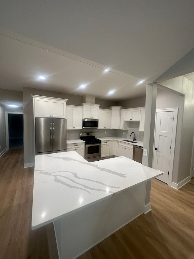 kitchen with appliances with stainless steel finishes, sink, light hardwood / wood-style flooring, white cabinets, and a center island