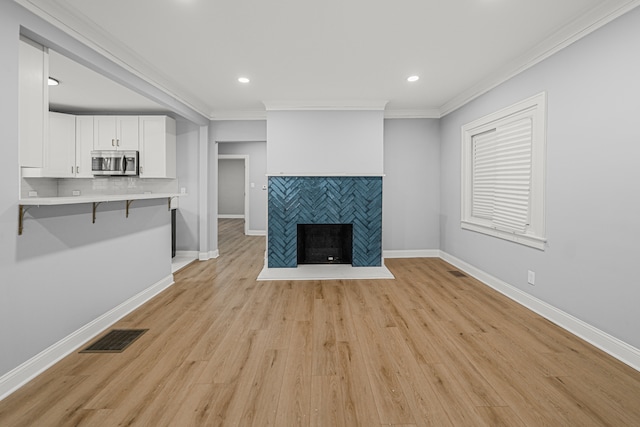 unfurnished living room with light hardwood / wood-style floors, crown molding, and a tiled fireplace