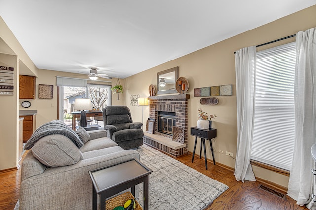 living room featuring hardwood / wood-style flooring, a brick fireplace, and ceiling fan