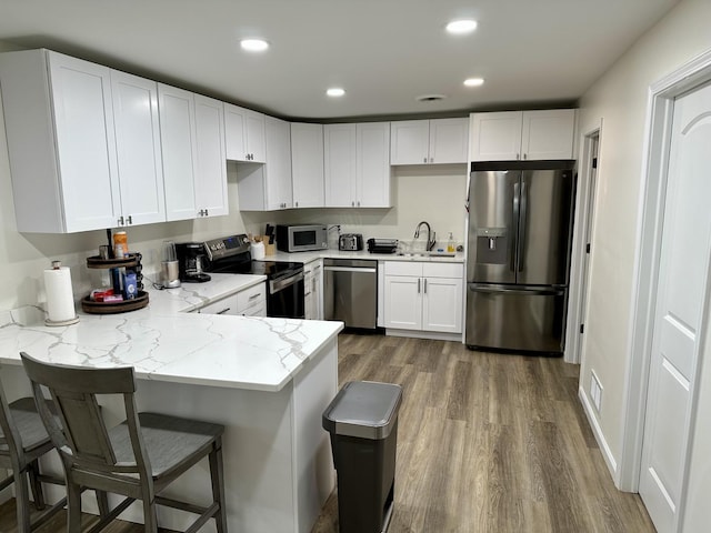 kitchen featuring hardwood / wood-style flooring, light stone countertops, white cabinetry, kitchen peninsula, and stainless steel appliances