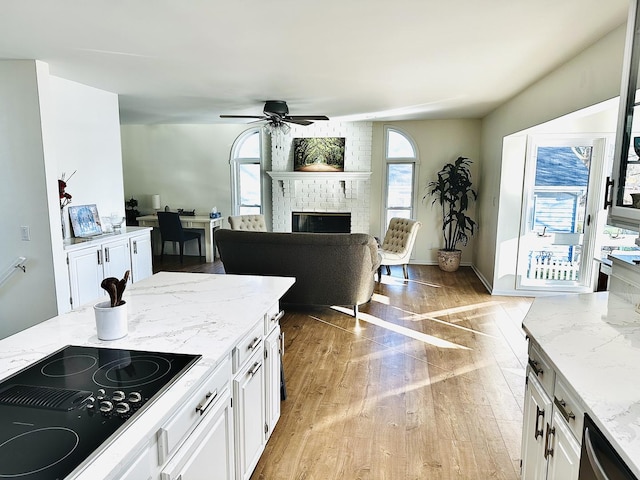 kitchen featuring white cabinets, ceiling fan, black electric cooktop, a fireplace, and light stone counters