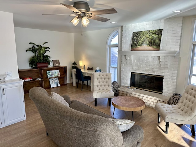 living room featuring ceiling fan, light hardwood / wood-style floors, and a brick fireplace