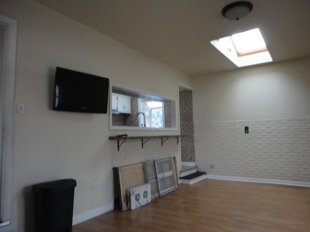 living room with hardwood / wood-style floors, sink, a skylight, and brick wall